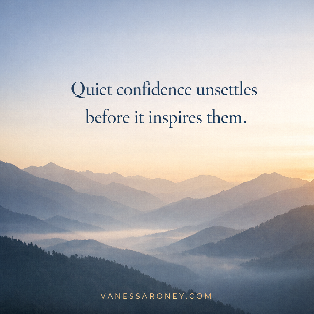 Minimalist quote graphic featuring a misty mountain sunrise in muted blue and gold tones with the words “Quiet confidence unsettles people before it inspires them” in elegant serif font and VanessaRoney.com at the bottom.